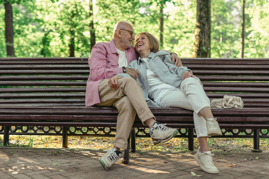 Older married couple sitting at a park bench together.